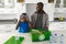 Happy african american son sorting recycling with father in kitchen, playing with plastic bottles