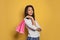 Happy african american woman holding pink shopping bags and smiling against vivid yellow background