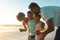 Happy african american woman sharing smartphone with family at beach during sunset