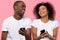 Happy african couple laughing using smartphones isolated on pink background
