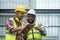 Happy African engineer and Asian foreman in helmets working at warehouse while listing problem on clipboard to discuss, inspect