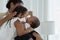 Happy African family, young mother and daughters, little kid older sister tender kissing her newborn baby sister hand