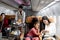 Happy African girl kid and woman passenger look at mobile phone during sit in comfortable seat inside airplane, female cabin crew