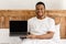 Happy African Guy Showing Laptop Screen Sitting In Bed Indoors