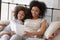 Happy african mother reading book relaxing in bed with daughter