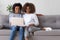 Happy african mother and teen daughter using laptop on sofa