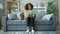 Happy Afro-American student reading book and smiling relaxing on couch at home