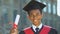 Happy afro-american teenage student in suit holding diploma, modern education