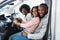 Happy Afro family sitting in new car, going on test drive, buying automobile in dealership store