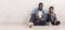 Happy afro father and son sitting on floor in similar pose