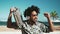 Happy Afro man having fun listening to music with wireless headphones and vintage boombox on the beach during summer