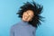 Happy Afro woman smiling, has good mood, dancing with her black curly hair flying, isolated on blue