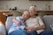 Happy aged spouses pensioners cuddle on sofa look at distance