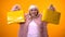 Happy aging lady in funny pink coat showing yellow shopping bags, wasting money