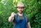 Happy agronomist man in gardening apron and hat pointing finger forward natural outdoors