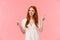 Happy alluring redhead female in white dress, helping out with fashion advices, pointing fingers left and right company