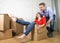Happy American couple unpacking moving in new house playing with unpacked cardboard boxes