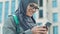 Happy Arab girl using smartphone, chatting with friends after classes in college