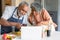 Happy arfican american senior couple preparing meal together and using laptop