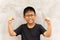 Happy Asian boy with glasses hands up and smiling over grey background.