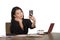 Happy Asian Chinese business woman taking selfie photo with mobile phone at corporate company office desk smiling playful in femal