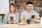 Happy asian couple in pajamas sitting at table in kitchen and watching video on mobile togerther at home in morning and having