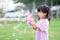 Happy Asian cute girl is playing a pink soap bubble gun. Child have fun playing on the lawn. A 4 year old children play outdoors.