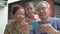 Happy Asian elderly grandparents watching video call from smartphone and cheerful adorable young granddaughter posing to camera.