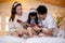 Happy asian family father and mother sitting teaching play ukulele guitar with daughter together on bed.