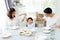 Happy Asian family raising child`s hands up and smiling while having a meal together.