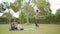 Happy asian father doing exercises on grass while mother and kid relaxing on yoga mat in park