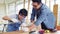 Happy Asian father and son work as a woodworker and carpenter. Father teaching his son to hammer nails on a wooden plank carefully