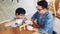 Happy Asian father and son work as a woodworker and carpenter. Father teaching his son to hammer nails on a wooden plank carefully