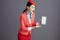happy asian female air hostess showing tablet PC against gray