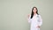 Happy Asian female doctor in uniform looking up, pointing finger up, standing over grey background