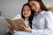 Happy asian girl reading book with her mother, sitting together on sofa and smiling, spending time at home interior