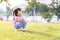 Happy Asian kid sitting squatting on the green lawn in the summer or spring time. Child making cute face and looking on top.