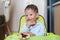 Happy Asian little baby boy sitting on children chair indoor eating bread with Stuffed Chocolate-filled dessert and Stained around