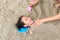 Happy asian little child girl buried in the sand at the beach by mother. Close-up kid playing with sand