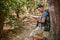 Happy Asian male trekker leaning on the tree and using smartphone while trekking in forest