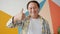 Happy Asian mature man smiling with thumbs-up hand gesture on colorful background