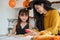 A happy Asian mom is decorating Halloween sandwiches with her little daughter in the kitchen