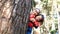 Happy Asian mother and daughter peeking out and smile from behind a tree at pine forest on winter day.