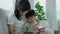 Happy Asian mother relax and read book with baby time together at home. parent sit on sofa with daughter and reading a story.