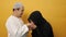 Happy Asian muslim couple doing greeting gesture, apologize and forgiving each other on eid mubarak tradition, against yellow