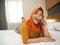 Happy Asian muslim woman wearing hijab talks on phone on her bed, young lady doing cellular communication concept