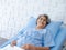 Happy Asian senior woman patient grey hair smiling and looking at camera while lying on bed in hospital.