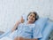 Happy Asian senior woman patient grey hair smiling, thumb up and looking at camera while lying on bed in hospital.