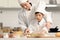 Happy Asian son and father in chef uniform with hat cook meal at kitchen, cute boy child kneads dough by rolling pin, dad helps