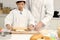 Happy Asian son and father in chef uniform with hat cook meal together at kitchen, cute boy kneads dough by rolling pin, parent